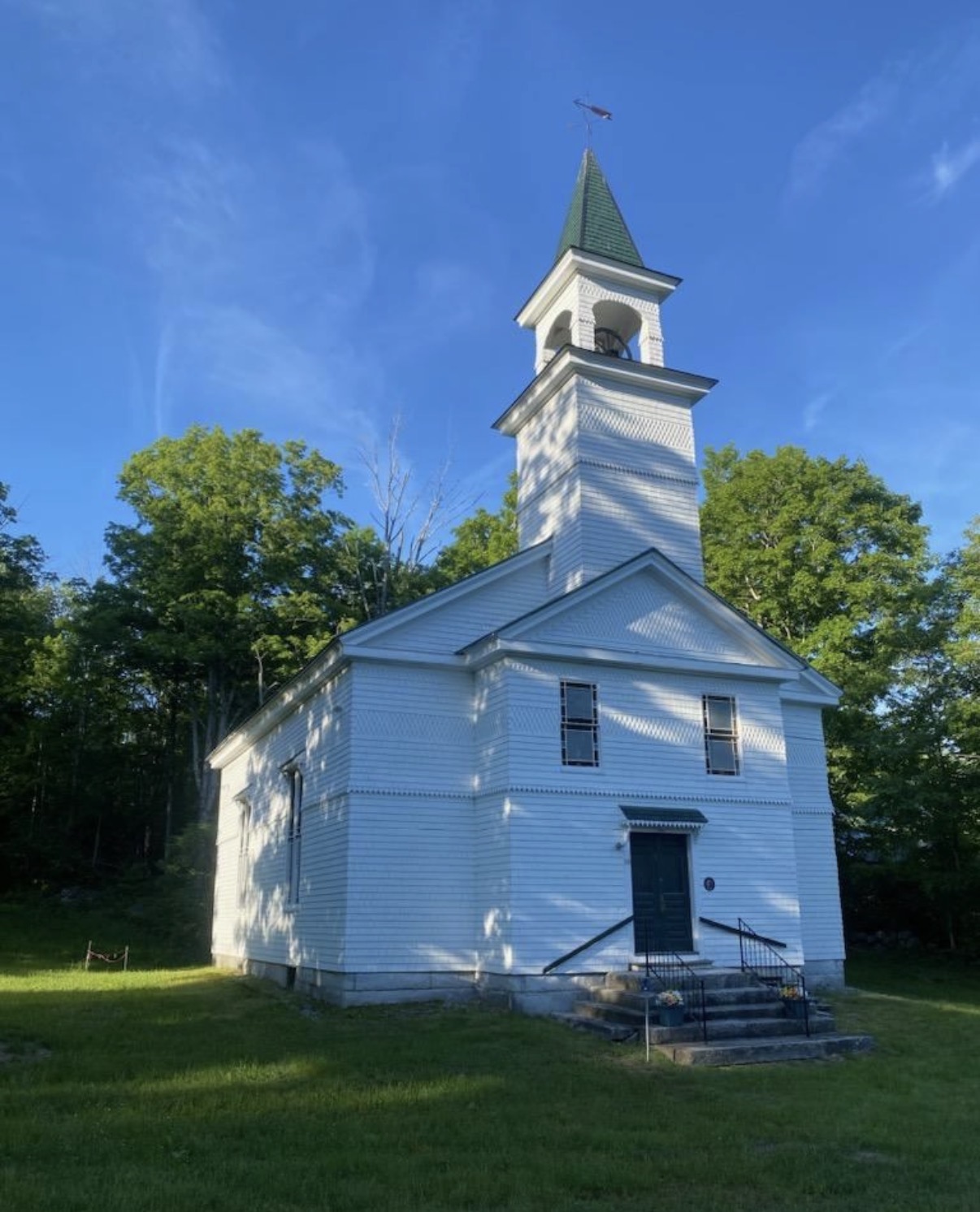 The white clapboard church building on Turnpike Road in Grafton, with its bell tower and green steeple against a blue sky