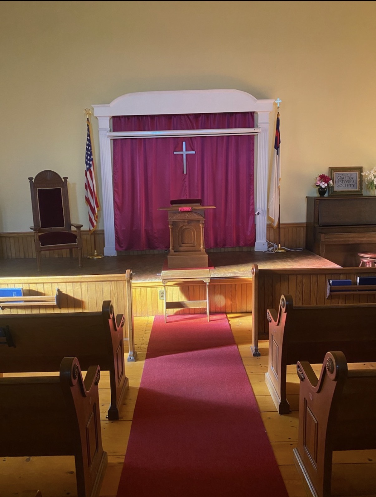 Inside the sanctuary: wooden pews on either side of a red aisle runner leading to the pulpit, with a cross on a crimson curtain behind it